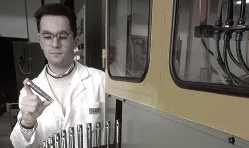 Man in lab coat holding tool near machinery