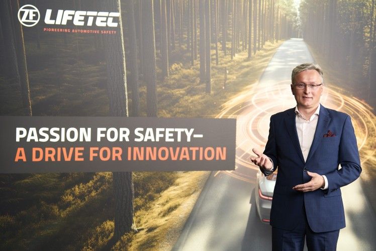 Man in suit presenting ZF Lifetec safety innovations, forest road background