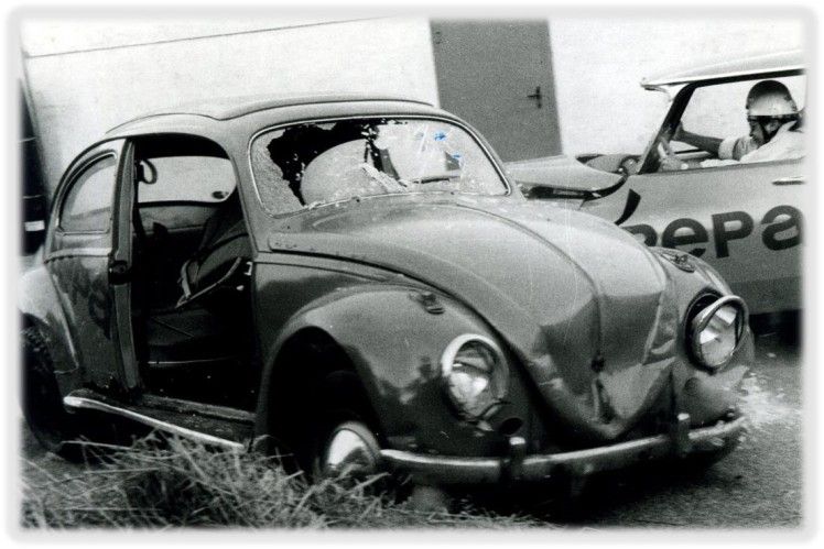 Damaged vintage Volkswagen Beetle with open door and shattered windows.