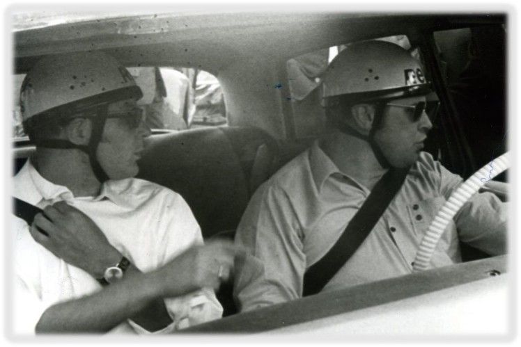 Two men wearing helmets and seat belts in a vehicle