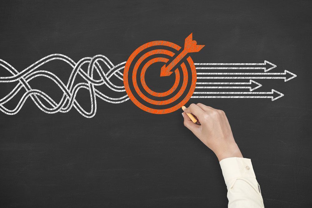 Hand drawing target with arrows on blackboard