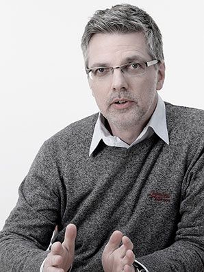 Man wearing glasses and a grey sweater with hands gesturing