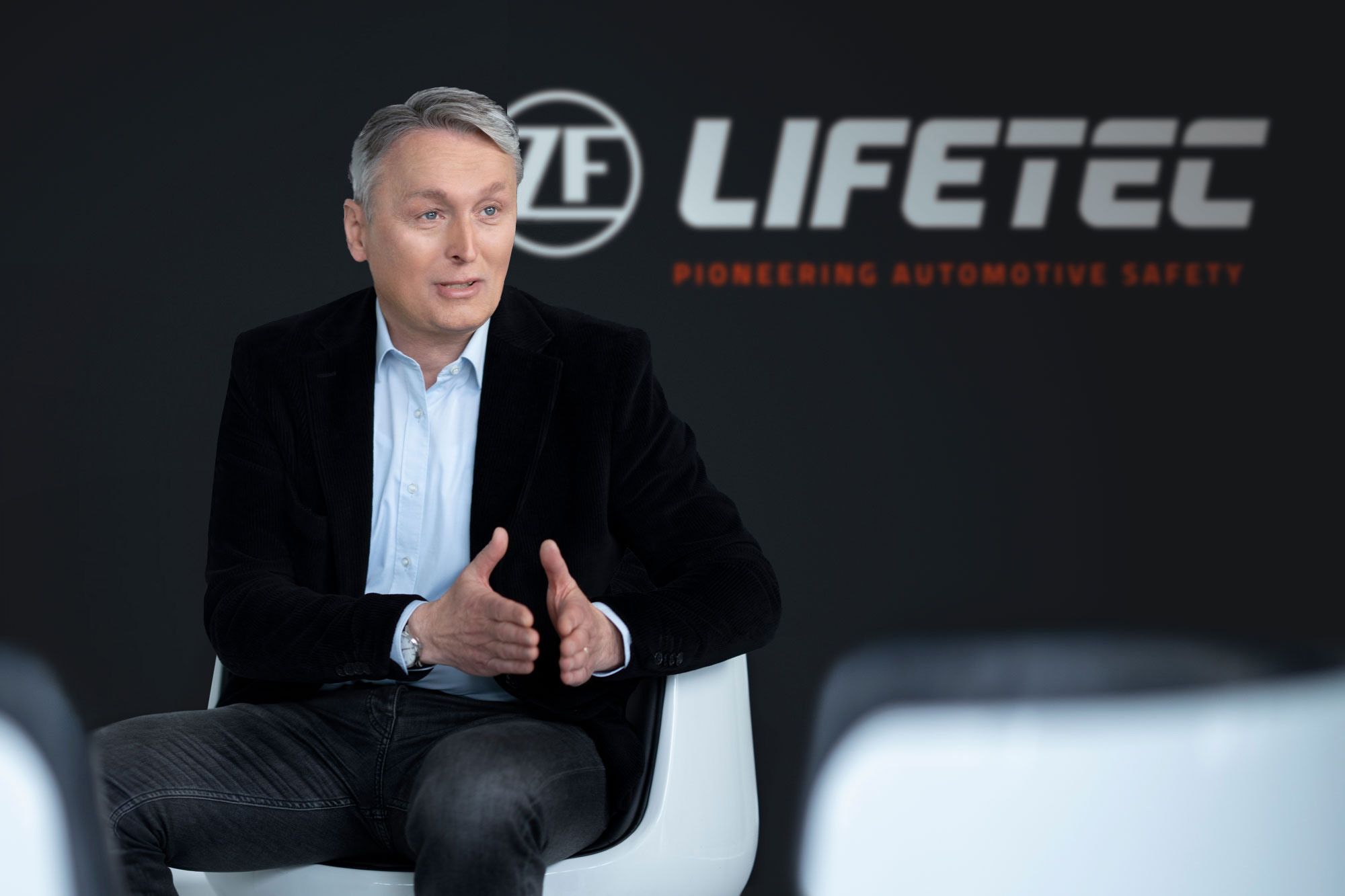 Man in suit speaking, LIFETEC logo behind