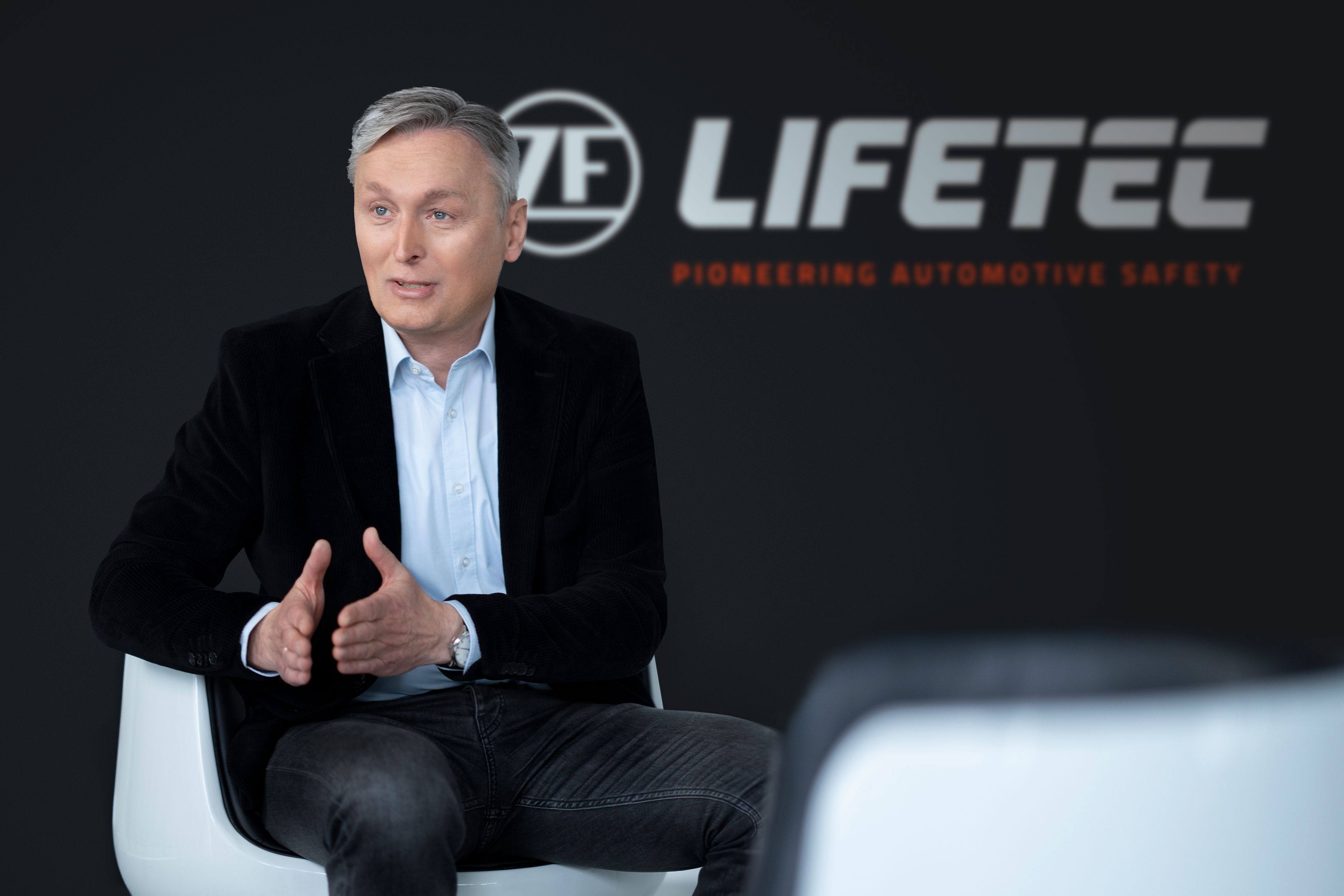Man in suit speaking, LIFETEC logo behind
